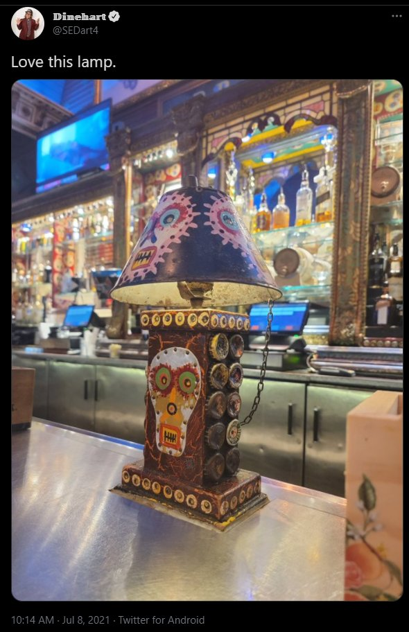 Screenshot of a tweet by Dinehart (@SEDart4):
"Love this lamp."
[A photo of a kitchy lamp decorated with bottlecaps, and sort of Mexican style cartoony skulls - clearly in a bar]